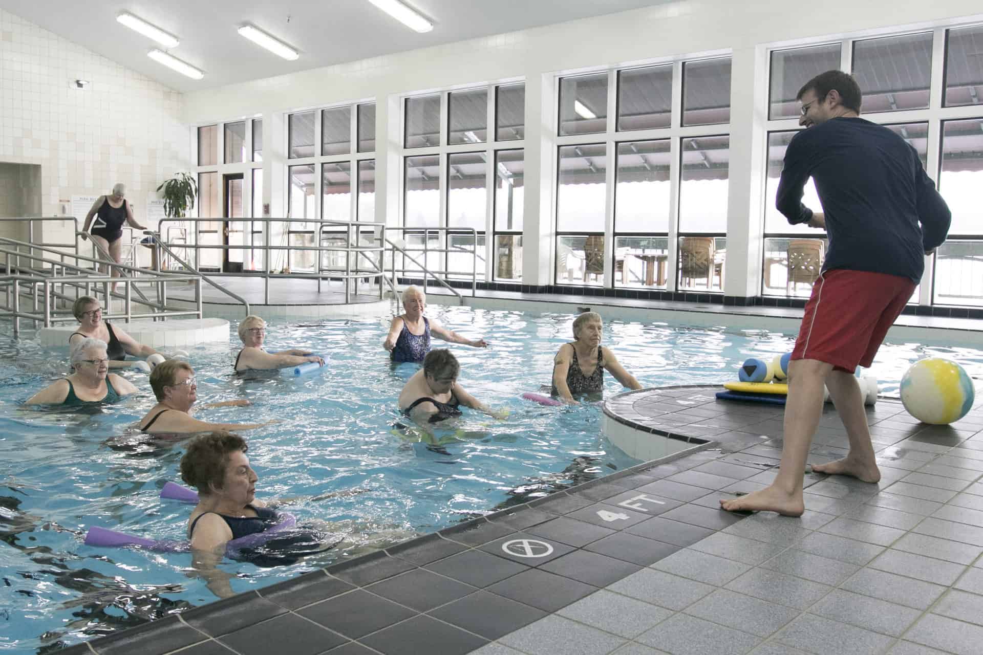 Copeland Oaks residents in a swimming pool doing water aerobics with an instructor.
