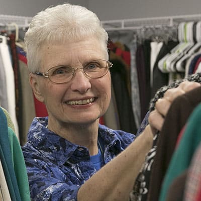 Older Woman smiling with racks of clothes around her