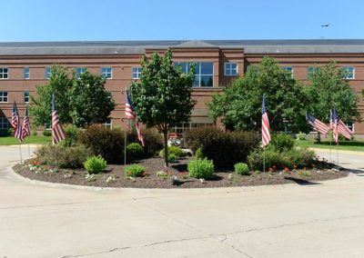 Large brown brick building with greenery and American Flags in front of it
