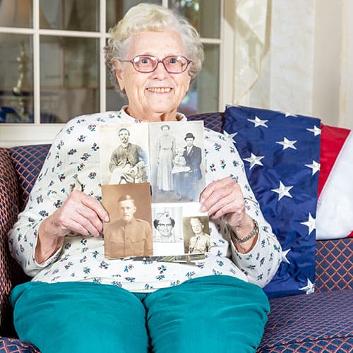 Older Woman smiling holding pictures of family members in uniform