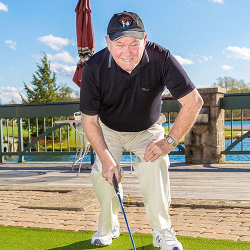 Older Gentleman bending down with golf club smiling