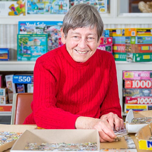 Older women smiling with many puzzles around her