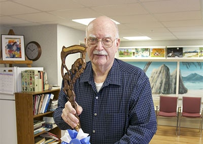 Older gentleman holding a wood carved item with a 1st place bow on it