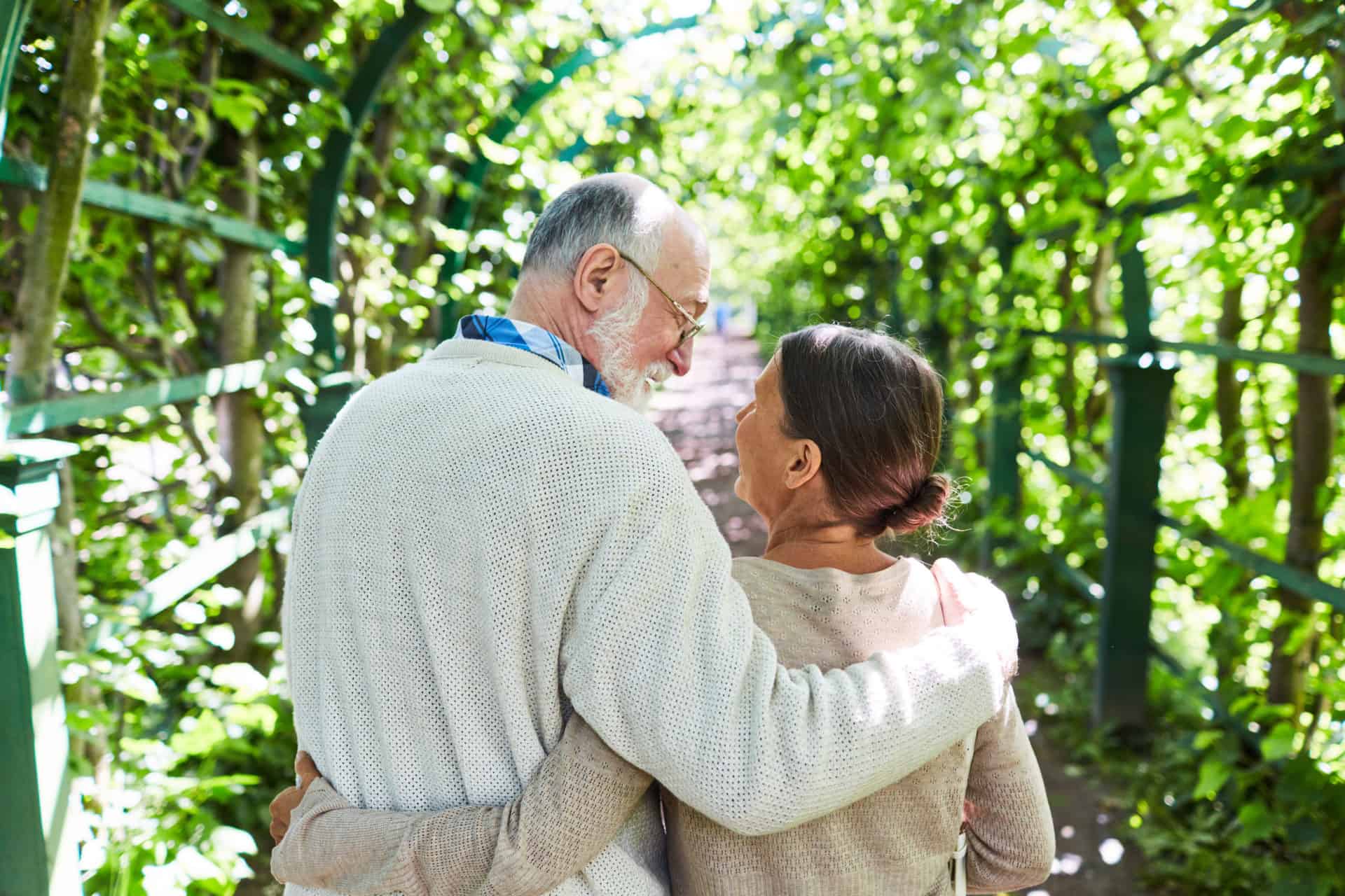 An elderly couple looking at each other smiling walking down a scenic bridge