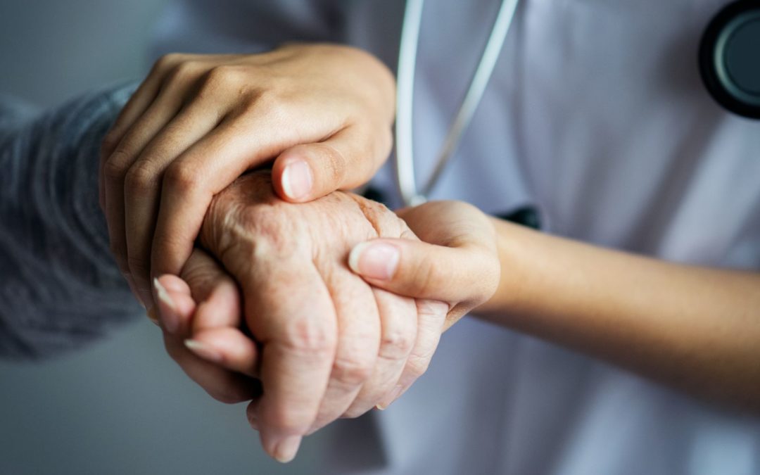 A doctor holding the hand of an elderly person.