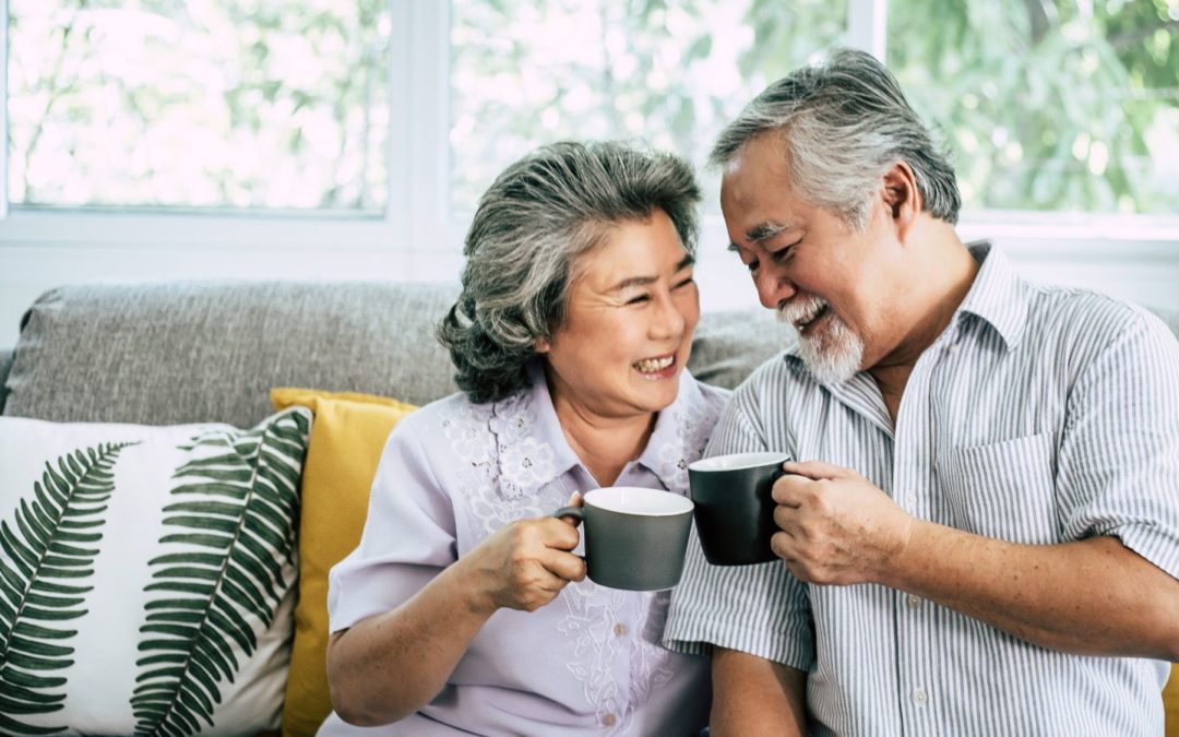 A senior couple sitting smiling at each other and drinking coffee.