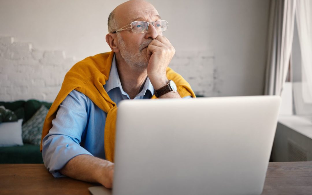 An older man ponding while using a laptop.
