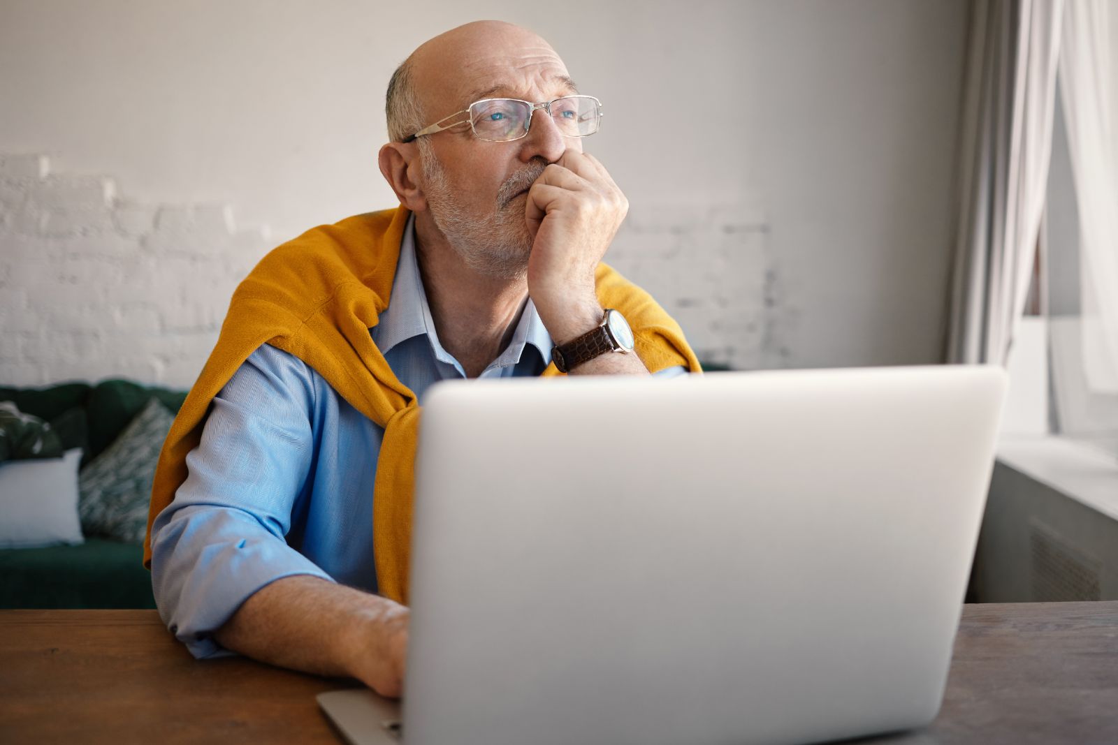 An older man ponding while using a laptop.