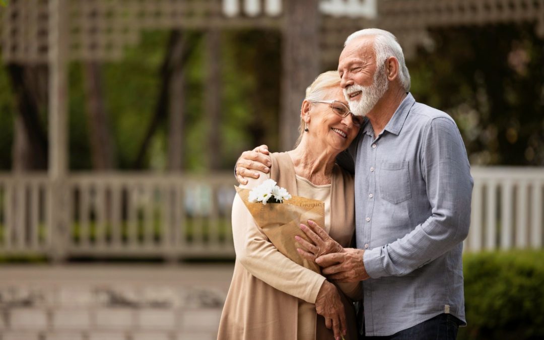 An elderly couple hugging and holding flowers.