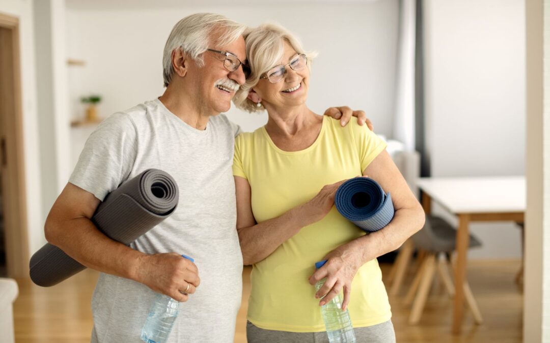 A happy elderly couple smiling with their yoga mats.